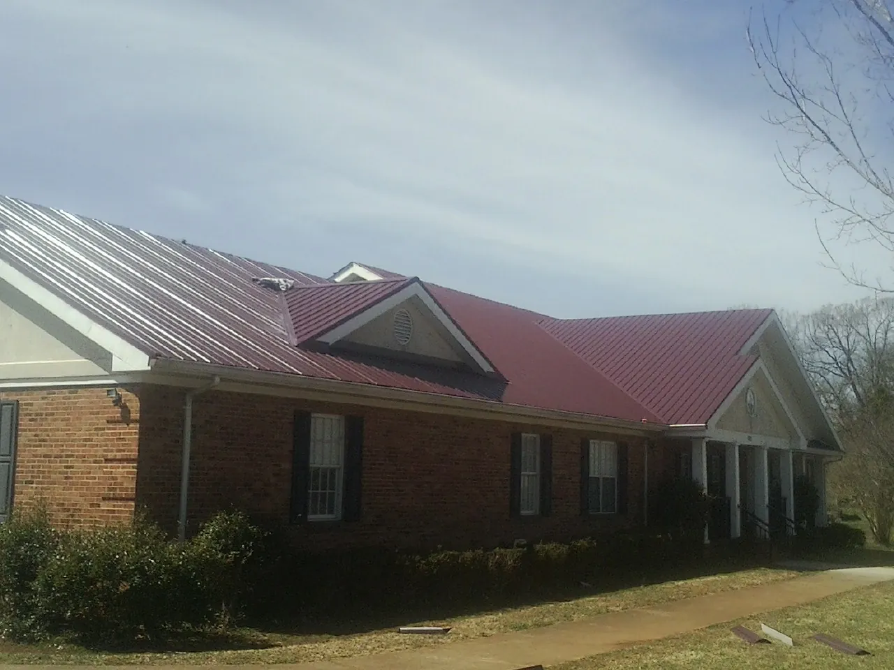 Red metal roof with gabled entries on a long brick building, from a Hail Damage Roof Repair job in Fabius