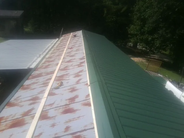 Old rusted panels beside newly installed green metal roofing — Wind Damage Roof Repair by Roofing Brothers in Fabius
