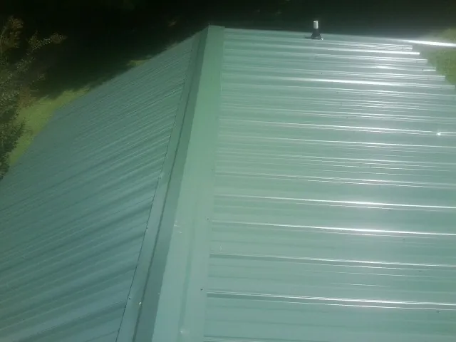 New green metal panels meeting at the ridge of a roof — Flat Roof Repair work by our crew in Fabius