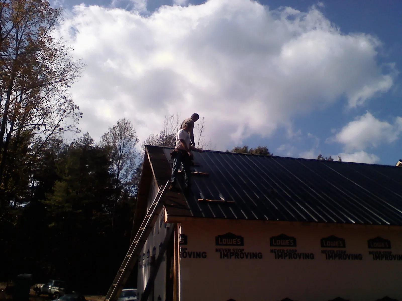 Roofer fastening dark metal panels high against a cloudy sky, from a Roof Inspection job in Fabius