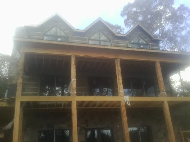 Dormers and porch framing on a large log home under construction — Roof Coating work by our crew in Fabius