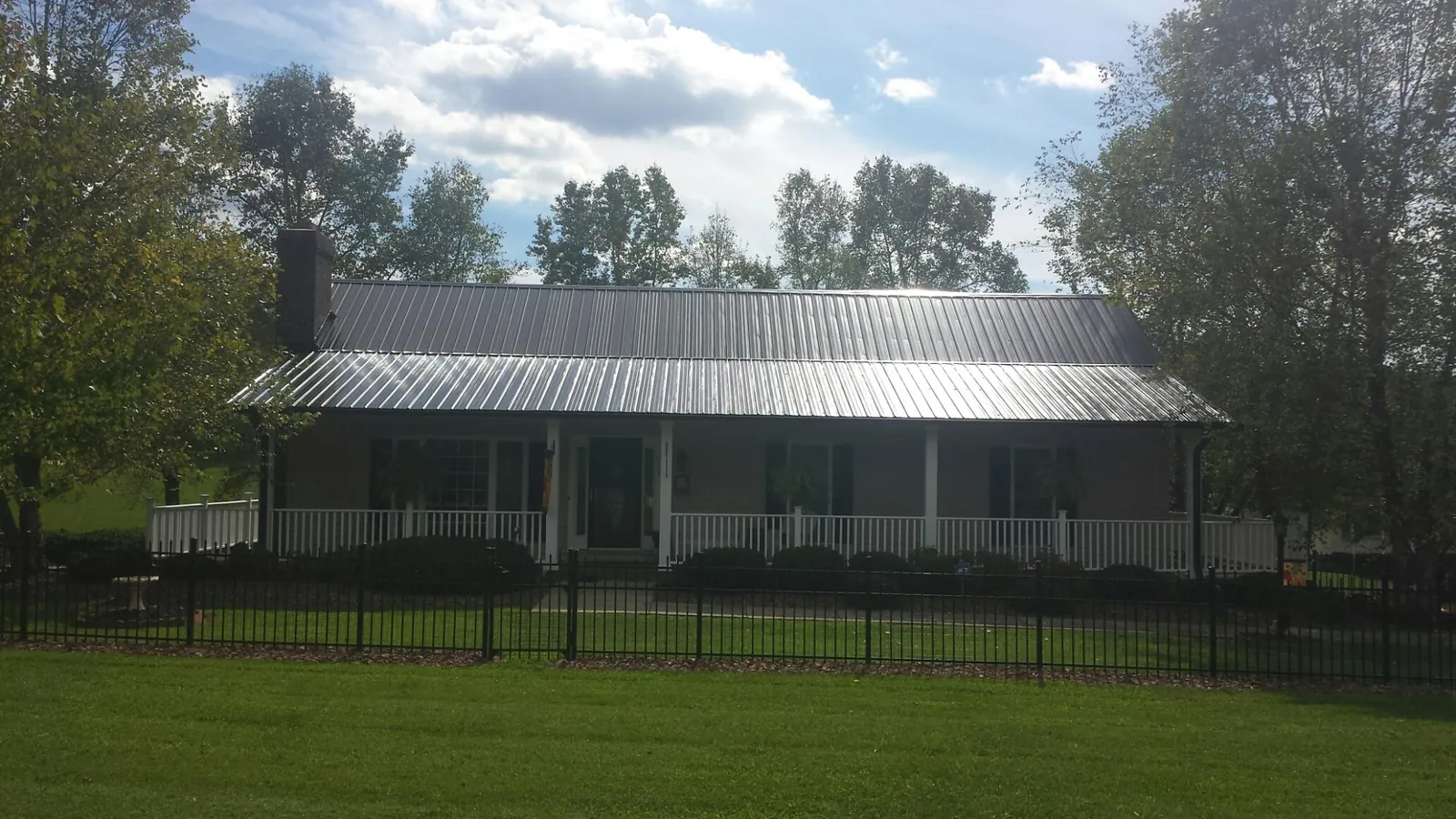 Gray metal roof on a brick ranch with a full width front porch — Gutter Guard Installation work by our crew in Fabius