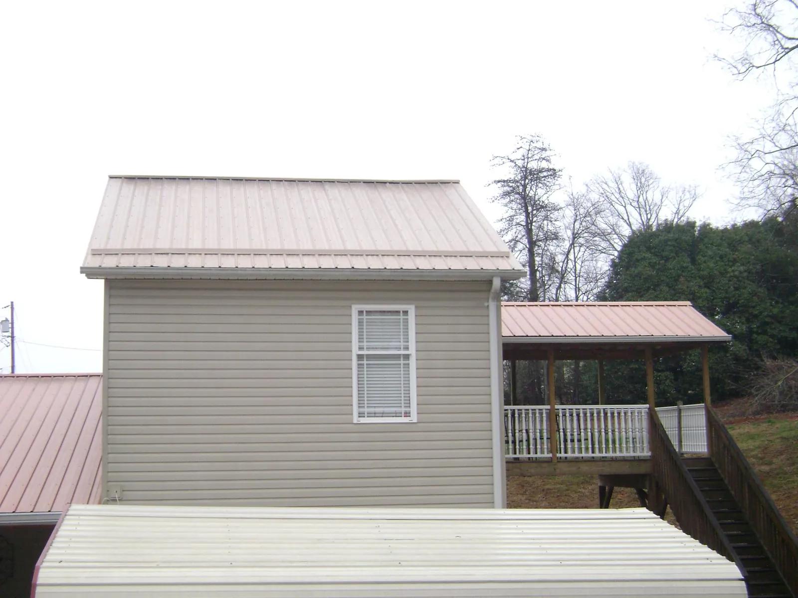 Tan metal roofs on a two story addition and attached porch, from a Roof Replacement job in Fabius